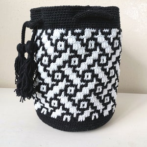 May include: Black and white crocheted bucket bag with black tassels. The bag has a geometric pattern.