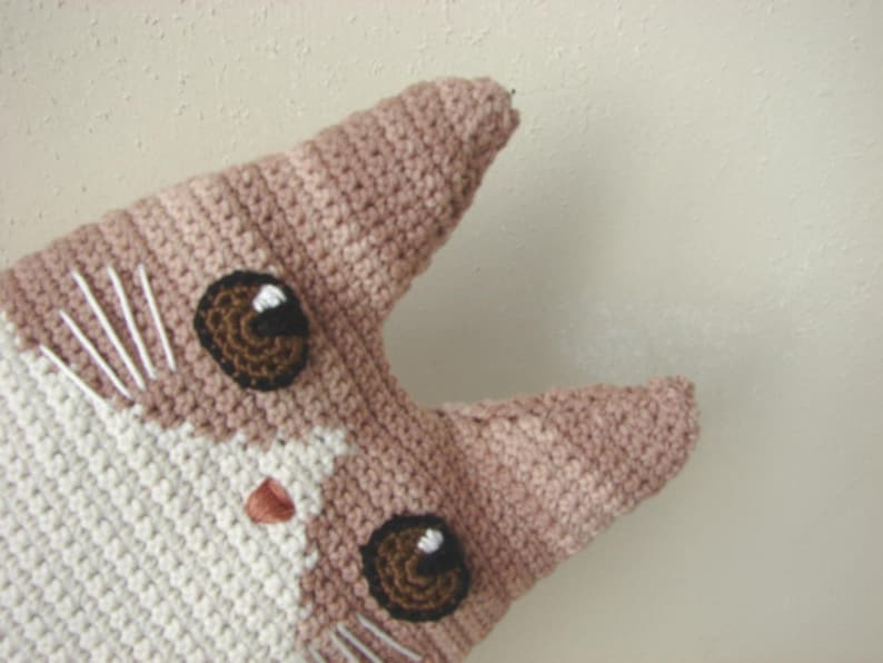 May include: A crocheted cat toy with brown eyes and a pink nose. The cat is made with white and pink yarn.