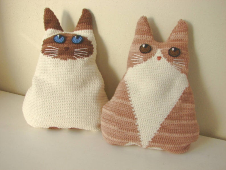 May include: Two crocheted cat plushies, one white with blue eyes and one brown and white with brown eyes.