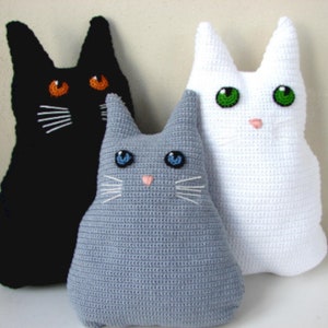 May include: Three crocheted cat plushies, one black, one gray, and one white. Each plush has embroidered facial features, including eyes, a nose, and whiskers.