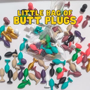 May include: A clear bag containing an assortment of small, brightly coloured butt plugs. The plugs are in shades of red, pink, green, blue, black, gold, and white. The text "LITTLE BAG OF BUTT PLUGS" is displayed above the bag.