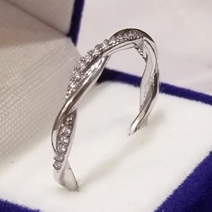 Puede incluir: Un anillo de banda de plata con un diseño trenzado y pequeñas piedras transparentes.