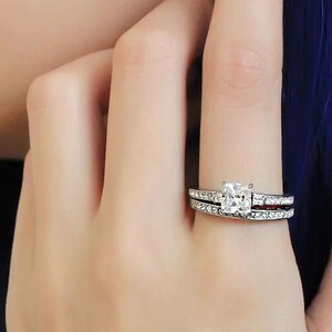 Puede incluir: Un anillo de plata con un diamante de forma cuadrada y una banda de diamantes m&aacute;s peque&ntilde;os.