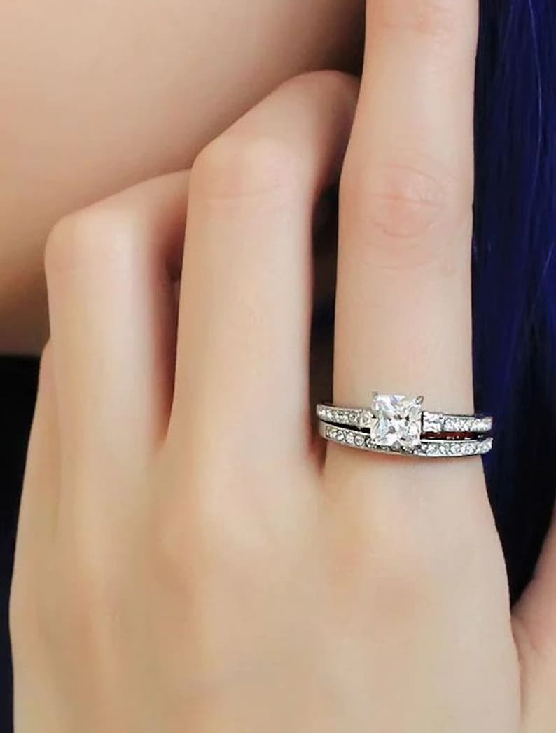 Puede incluir: Un anillo de plata con un diamante de forma cuadrada y una banda de diamantes m&aacute;s peque&ntilde;os.
