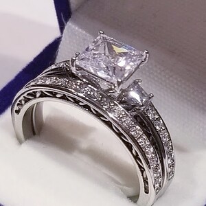 Puede incluir: Un anillo de compromiso de plata con un gran diamante de talla coj&iacute;n y una banda de diamantes m&aacute;s peque&ntilde;os.