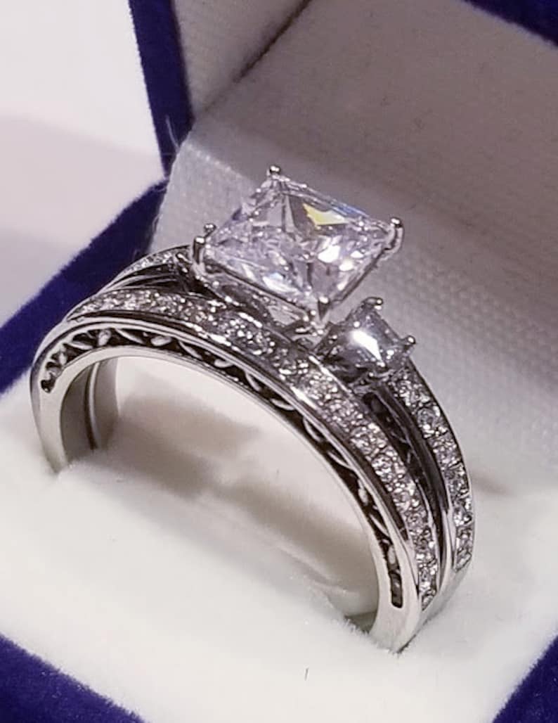 Puede incluir: Un anillo de compromiso de plata con un gran diamante de talla coj&iacute;n y una banda de diamantes m&aacute;s peque&ntilde;os.