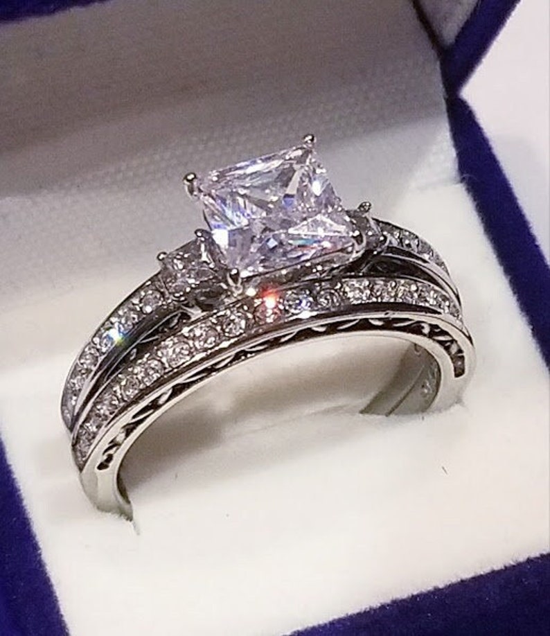 Puede incluir: Un anillo de compromiso de plata con un gran diamante de talla coj&iacute;n y una banda m&aacute;s peque&ntilde;a de diamantes.