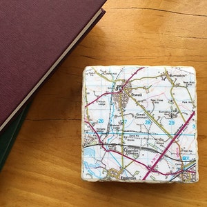 May include: A white ceramic coaster featuring a map of Etwall, England. The map depicts roads, streets, and local landmarks. The coaster is square-shaped and has a white background with black lines and text.