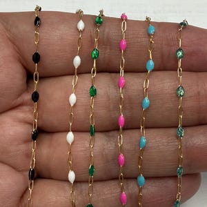 May include: Six gold chains with different colored beads. The beads are oval shaped and are black, white, green, pink, and blue.