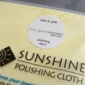 Könnte beinhalten: Ein gelbes Poliertuch mit dem Text "SUNSHINE® POLISHING CLOTH" und "Keep your jewelry Safely clean". Ein weißer runder Aufkleber mit dem Text "silver & gold lime green modern etsy.com polishing cloth" befindet sich auf dem Tuch.