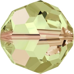 Op de afbeelding: Een lichtgroene gefacetteerde glazen kraal met een gouden iriserende afwerking. De kraal heeft een gat in het midden om te rijgen.