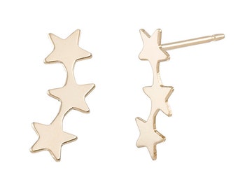 May include: A pair of gold-toned star stud earrings. Each earring features three stars stacked vertically.