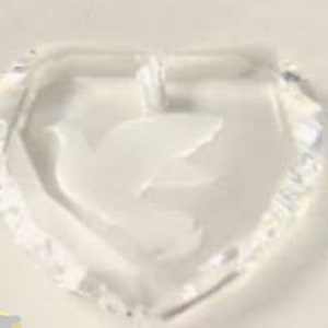May include: A clear crystal heart-shaped ornament with a white dove design inside. The ornament has a small loop at the top for hanging.
