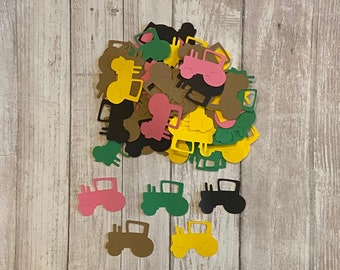 May include: A pile of paper cutouts of tractors in various colors, including pink, yellow, green, and brown. The cutouts are scattered on a wooden surface.