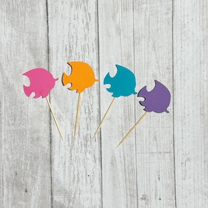 May include: Four colorful fish-shaped paper cutouts on wooden sticks. The fish are pink, orange, teal, and purple.