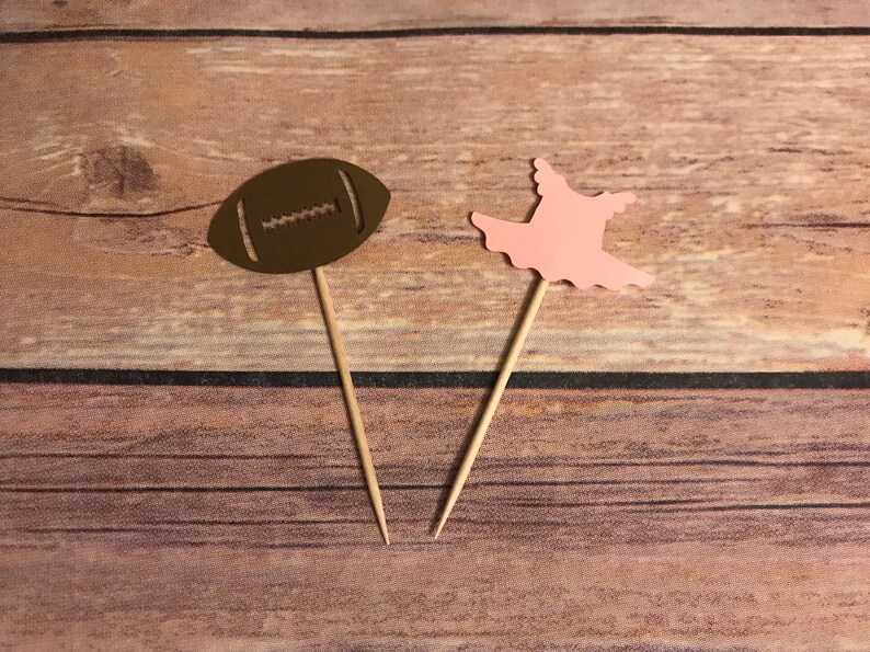 Op de afbeelding: Twee cupcake-toppers, een in de vorm van een bruine voetbal en de andere in de vorm van een roze ballerina-jurk.