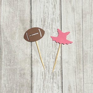 Op de afbeelding: Twee cupcake-toppers, een in de vorm van een bruine voetbal en de andere in de vorm van een roze tutu.