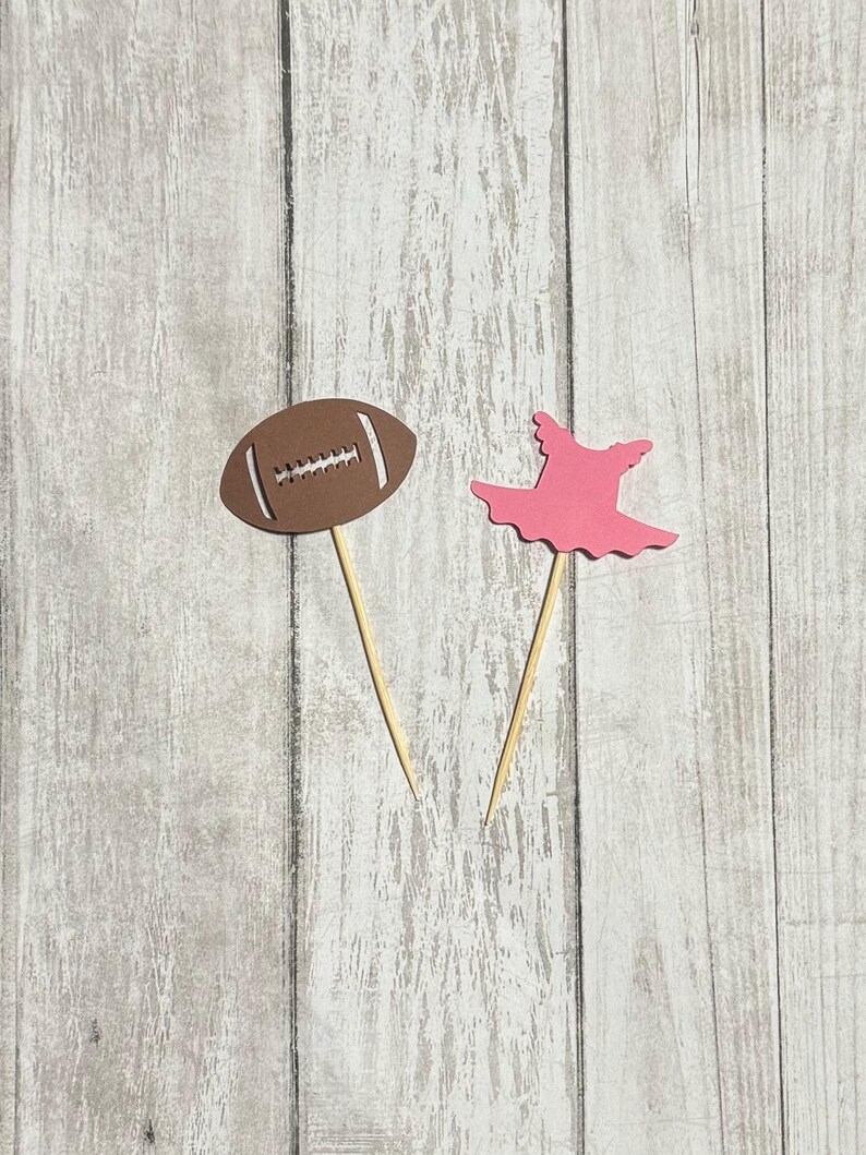 Op de afbeelding: Twee cupcake-toppers, een in de vorm van een bruine voetbal en de andere in de vorm van een roze tutu.