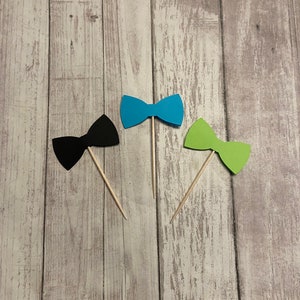 May include: Three paper bow ties on wooden sticks. The bow ties are black, blue, and green.