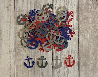 May include: A pile of paper anchor confetti in red, blue, and gray. The anchors are scattered on a light wood background. There are four larger anchors at the bottom of the image, one in each color.