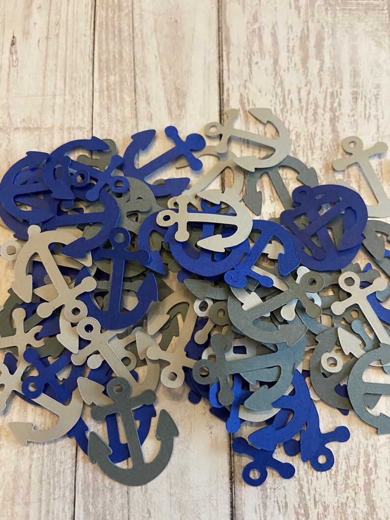 Puede incluir: Un mont&oacute;n de confeti de papel en forma de ancla de color azul y gris. Las ancras son de varios tama&ntilde;os y formas.
