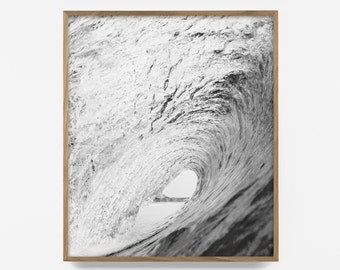 May include: Black and white photograph of a large wave breaking, creating a tunnel-like shape. The wave is framed by a wooden frame.