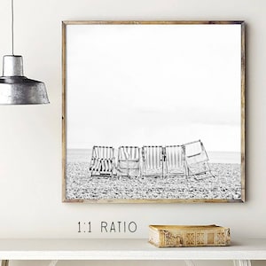 Puede incluir: Fotograf&iacute;a en blanco y negro de cinco sillas de playa a rayas en una playa de arena. Las sillas est&aacute;n dispuestas en fila, mirando hacia el oc&eacute;ano. La foto est&aacute; tomada desde un &aacute;ngulo bajo, por lo que las sillas parecen altas e imponentes.