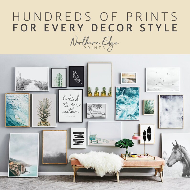 May include: A gallery wall with a variety of framed prints, including a pineapple, a wave, a cactus, a feather, a palm tree, a beach scene, and a quote that says "Be kind to one another". The wall is painted a light gray and the frames are all white. There is a pink bench in front of the wall with a white fur throw on top.