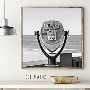 May include: Black and white photograph of a vintage coin-operated telescope on a boardwalk overlooking the ocean.