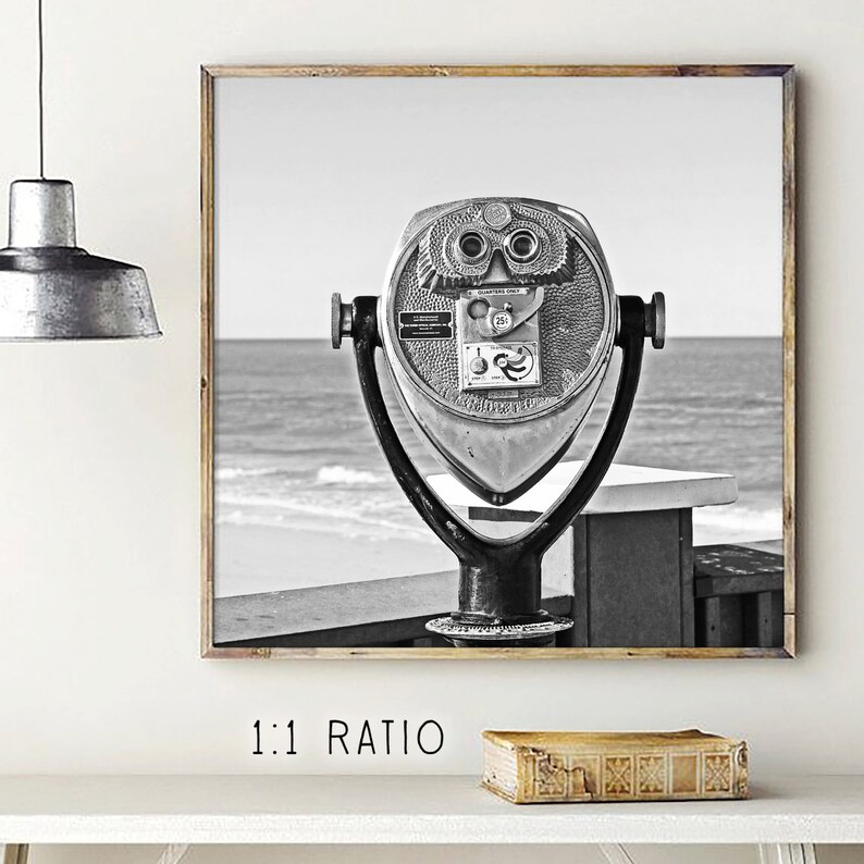 May include: Black and white photograph of a vintage coin-operated telescope on a boardwalk overlooking the ocean.