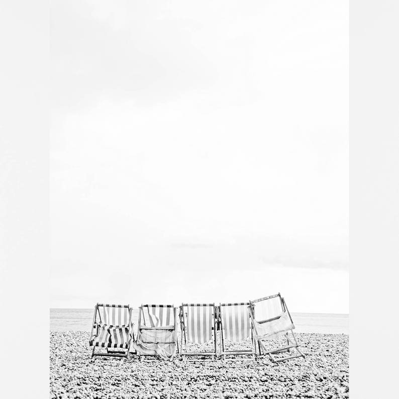 Puede incluir: Cinco sillas de playa a rayas blancas y negras est&aacute;n alineadas en una playa de guijarros. Las sillas est&aacute;n plegadas y mirando hacia el oc&eacute;ano.