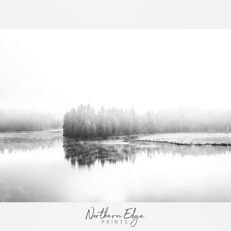May include: Black and white landscape photograph featuring a tranquil lake reflecting a forested island. The image is shrouded in mist, creating a soft, ethereal atmosphere. The text "Northern Edge Prints" is at the bottom.