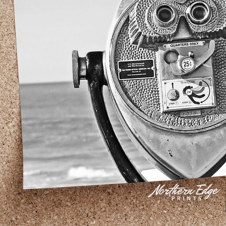 May include: A black and white photo of a vintage coin-operated viewer with the text "Quarters Only" and "To Operate" on the side. The viewer is pointed towards a body of water.