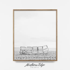 Puede incluir: Fotograf&iacute;a en blanco y negro de una fila de seis sillas de playa a rayas en una playa de guijarros. Las sillas est&aacute;n mirando hacia el oc&eacute;ano y el cielo est&aacute; nublado.