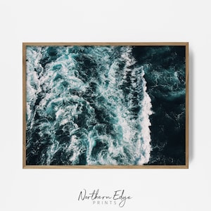 May include: An aerial view of a deep blue ocean with white foamy waves crashing against each other. The water is a vibrant teal colour and the waves are a stark white.