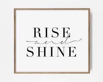 May include: A framed print with a white background and black text that reads "RISE and SHINE".