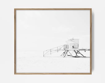 Puede incluir: Fotografía en blanco y negro de una caseta de salvavidas en una playa. La caseta es una estructura simple con una escalera que lleva hasta la cima. La playa está vacía y el cielo está nublado.