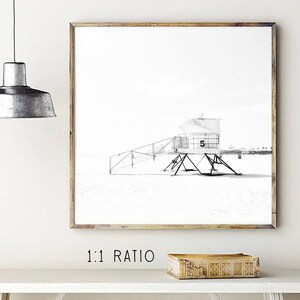 May include: Black and white photograph of a lifeguard stand on a beach. The stand is numbered "5" and has a ladder leading up to the top. The beach is empty and the sky is clear.