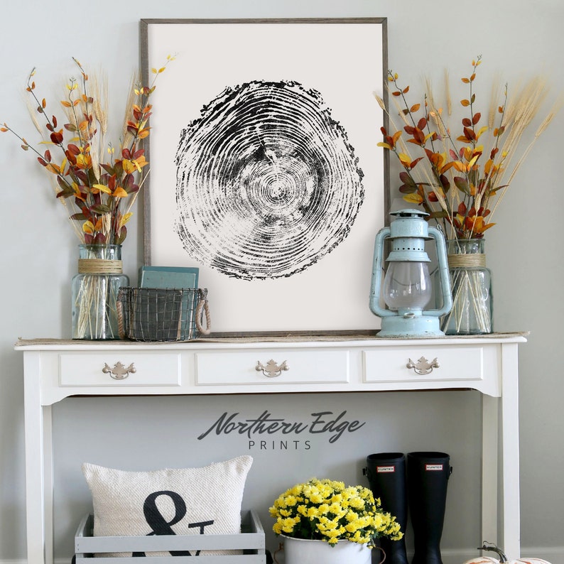 May include: A framed black and white tree ring print is the focal point of a decorative display. The print is on a white background. The display includes a light blue lantern, vases with fall foliage, and a white console table. The text "Northern Edge Prints" is visible.