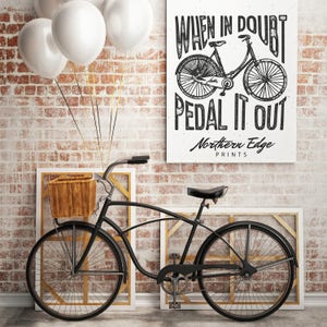 K&ouml;nnte beinhalten: Schwarzwei&szlig;-Illustration eines Fahrrads mit dem Text "When in doubt pedal it out" und "Northern Edge Prints". Ein schwarzes Fahrrad mit einem Korb lehnt an einer Backsteinwand mit wei&szlig;en Luftballons.