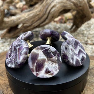 May include: Five amethyst gemstone cabinet knobs with gold metal hardware. The knobs have a variety of purple and white patterns.