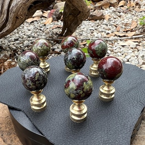 May include: Eight red, green, and black gemstone finials with gold bases. The finials are arranged on a black surface.