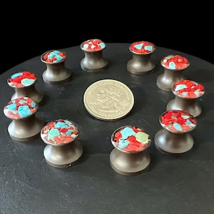 Könnte beinhalten: Braune Ohrstecker mit Mosaikoberflächen in Rot, Türkis und Grün. Eine amerikanische Vierteldollarmünze dient zum Größenvergleich. Die Ohrstecker sind kreisförmig auf einer dunklen Oberfläche angeordnet.