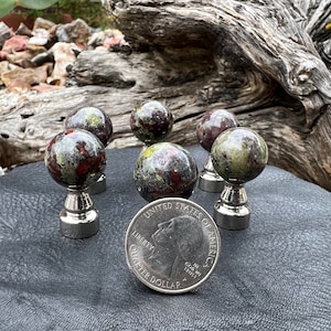 Może przedstawiać: Pięć małych, okrągłych, zielonych, czerwonych i czarnych kamieni ozdobnych z podstawami ze srebra. Kamienie są mniej więcej wielkości amerykańskiej monety 25 centów.