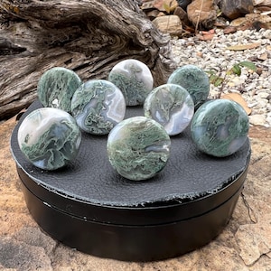 Pode incluir: Uma caneca de cerâmica branca com uma alça preta e o texto "But First, Coffee" em preto, em negrito. A caneca está sobre uma superfície de madeira. A caneca tem aproximadamente 10 cm de altura.