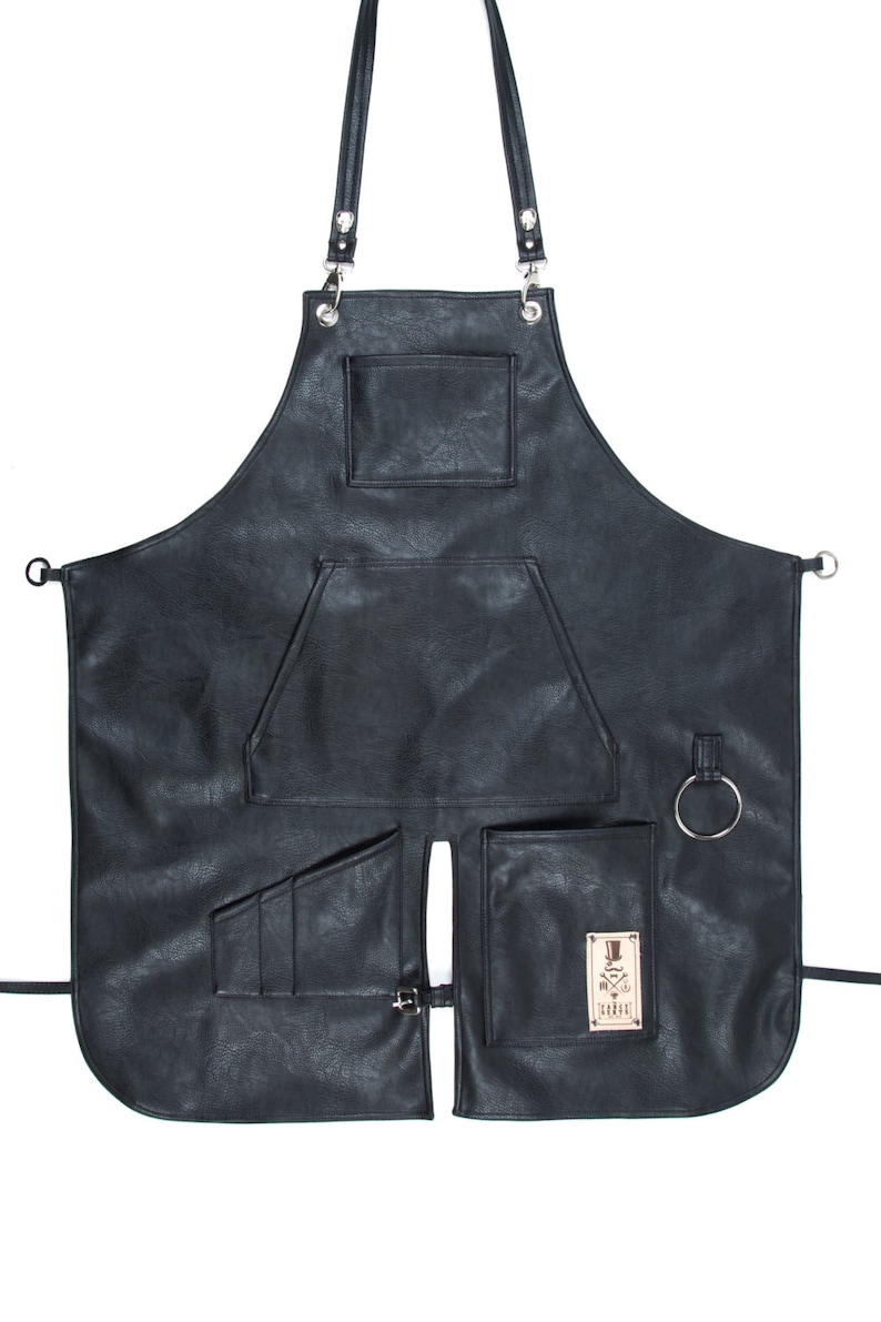 May include: Black leather apron with multiple pockets and a logo that says "The Barber" with a crossed razor and top hat design.