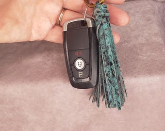 May include: A teal blue leather tassel keychain with a silver key fob attached to a brass key ring.