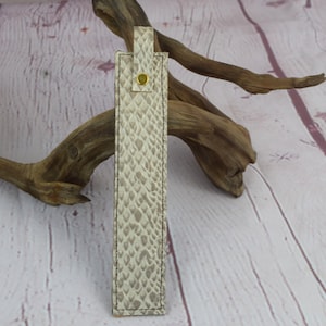 May include: A beige leather bookmark with a snakeskin pattern and a gold button.