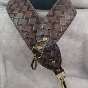 May include: A brown leather strap with a woven pattern and gold-toned hardware. The strap has two swivel clips.