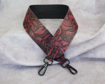 May include: A red leather camera strap with a black floral pattern and black metal clasps.